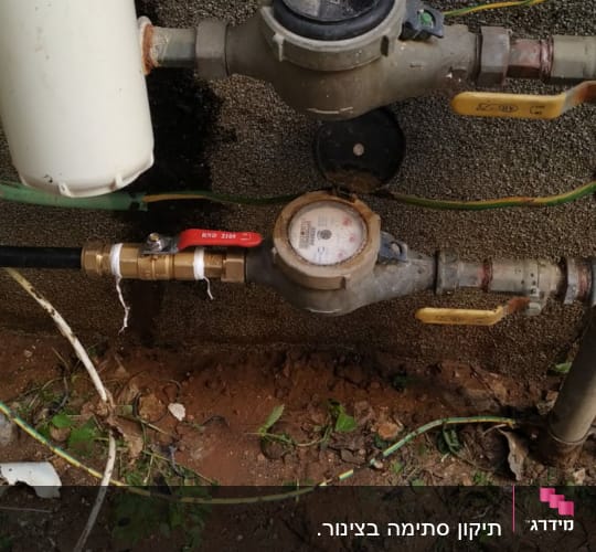 מד מים עם צינורות וברזים מחוברים לקיר